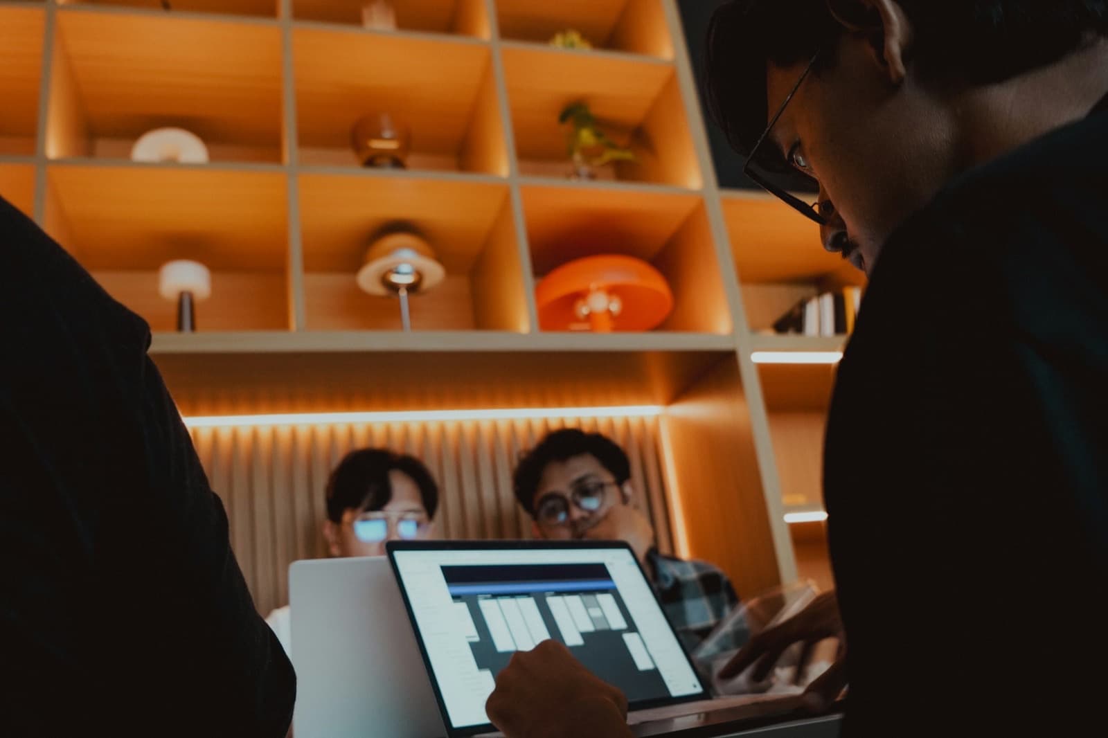 Three colleagues around a laptop in warm light, one pointing at the screen