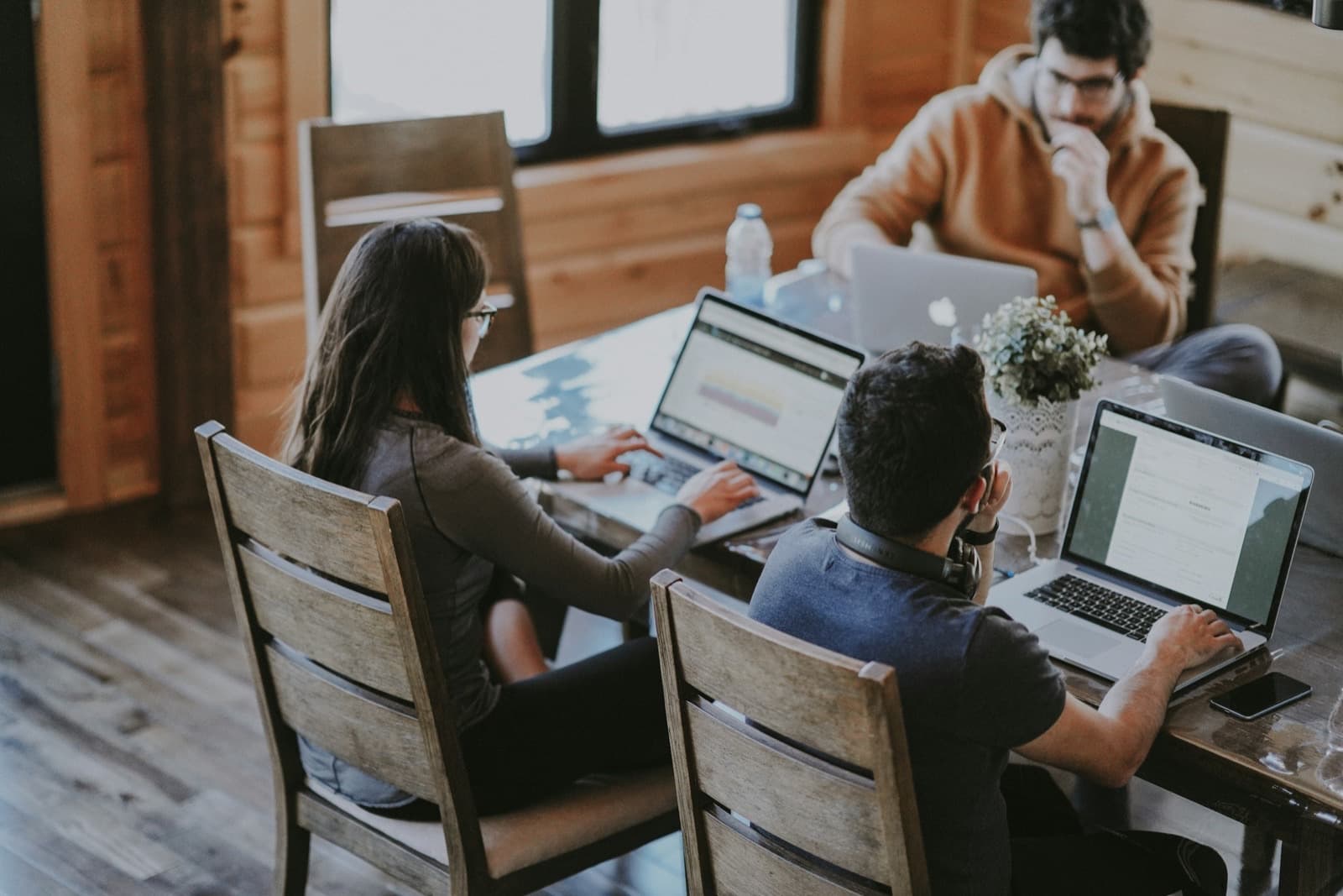 Three people working on laptops at a wooden table