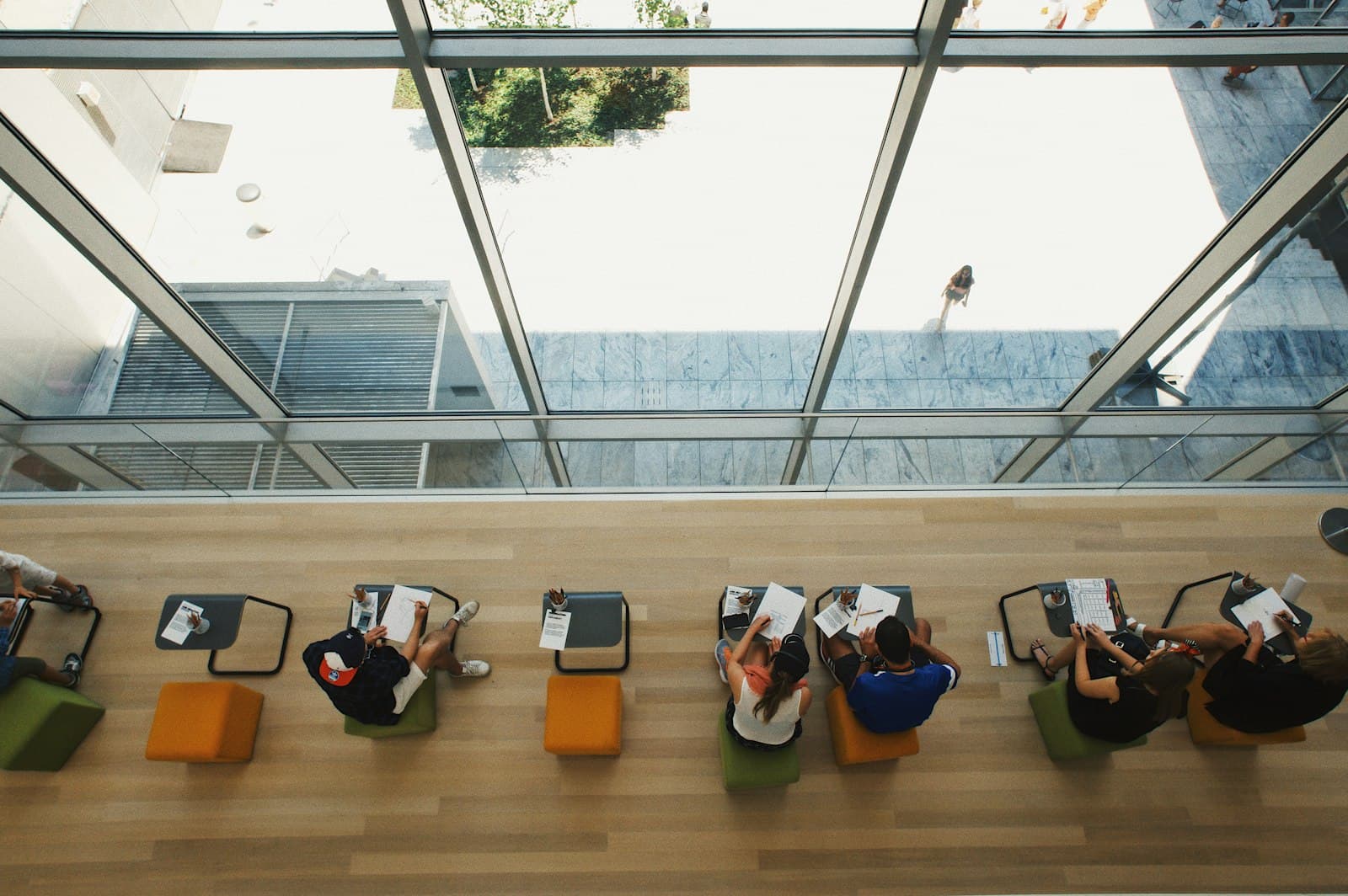 People reading and working at a long counter beside a window, seen from above