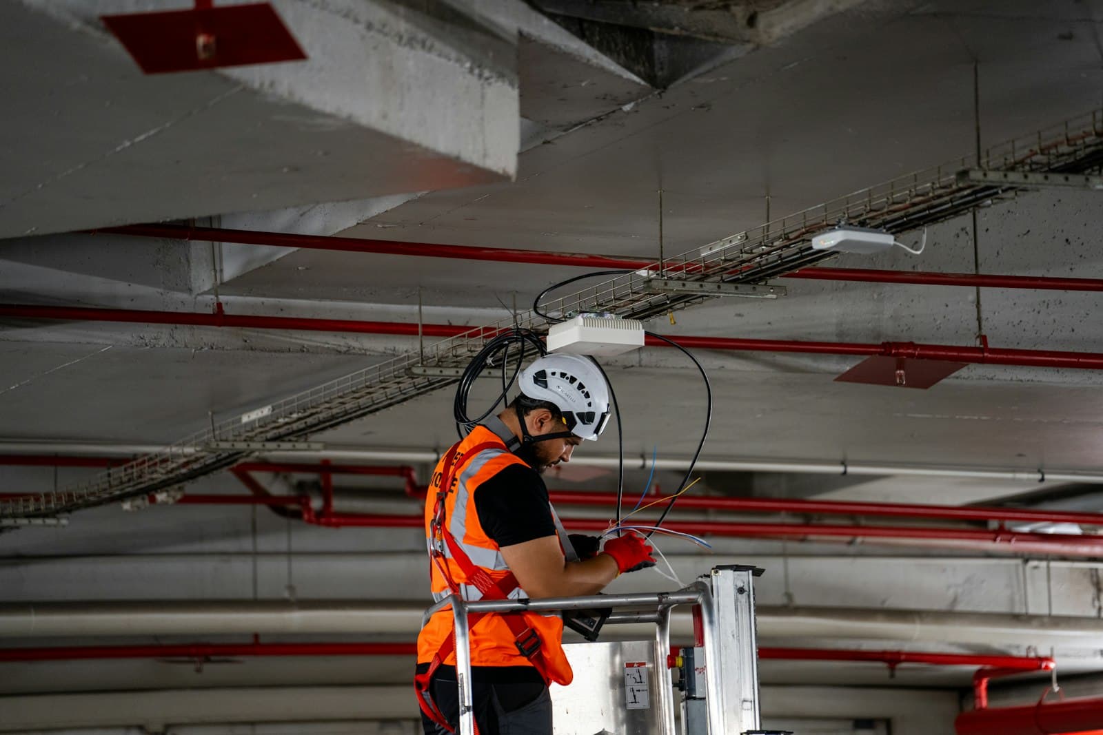 A worker in a safety vest and helmet working on pipes under a ceiling